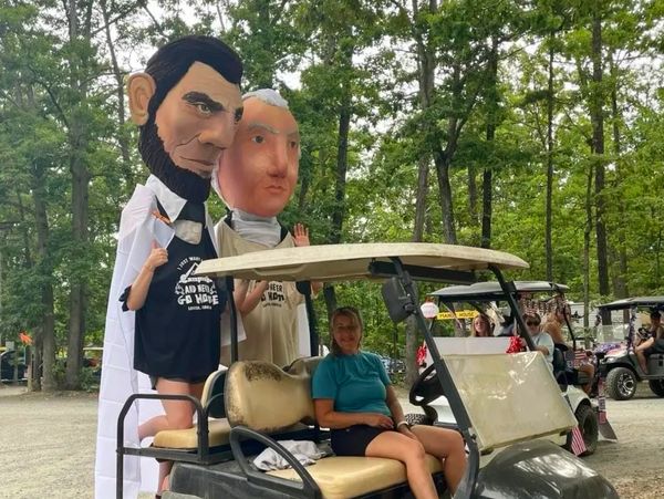 A huge Abe Lincoln and George Washington head hitch a ride on the back of a golf cart.