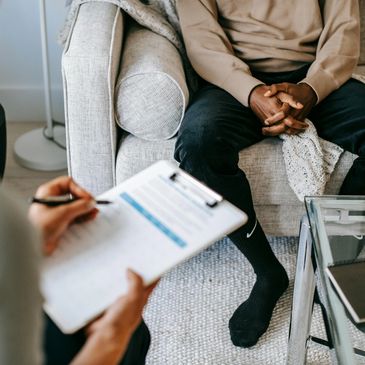Man sitting on couch while women sits across from him writing on a clip board