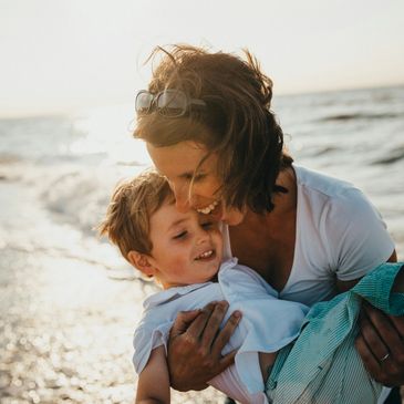 A mother holding her son while laughing at the beach on a sunny evening