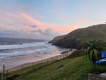 Sunset over a peaceful beach with blue lounge chairs and a wooden house.