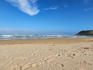 Sunny beach with waves and a distant green hill on a clear day.