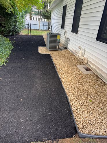 Neatly landscaped side yard with black mulch and tan gravel around HVAC unit.