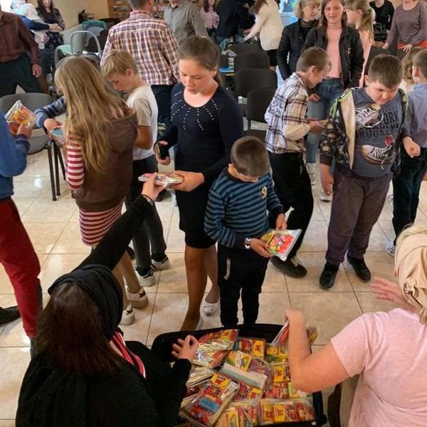 Children receiving colorful books or booklets in a community setting.