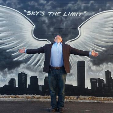 Man posing with outstretched arms in front of angel wings mural.