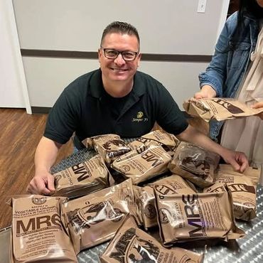 Man smiling with several MRE food packages on a table.