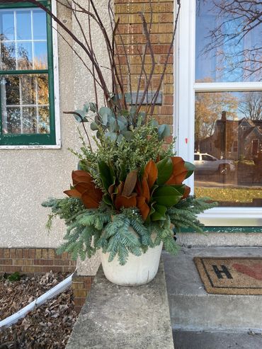 Winter pot decorated with willow, eucalyptus, magnolia, spruce tops, and lights.