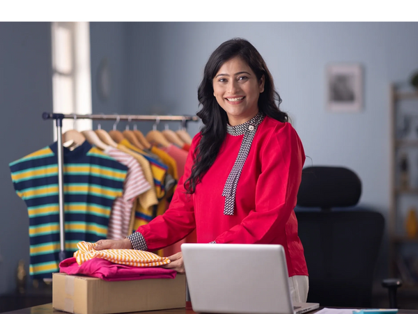 Smiling woman with folded clothes in a bright room with hanging shirts.