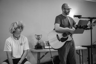 Man playing guitar and boy sitting beside a trophy on a table.