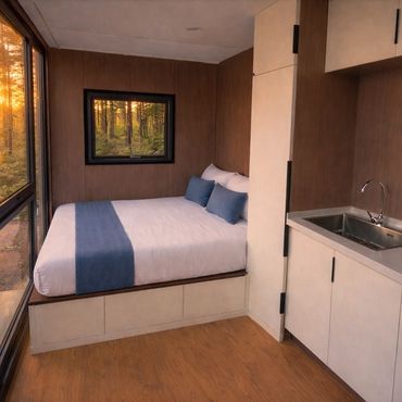 Cozy modern bedroom with large windows overlooking a forest at sunset.