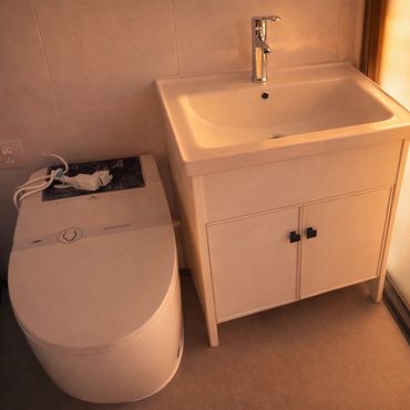 Compact modern bathroom with a toilet and sink cabinet in soft warm lighting.