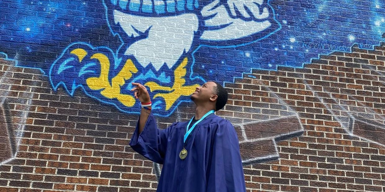 Graduate pointing up in front of colorful eagle mural.