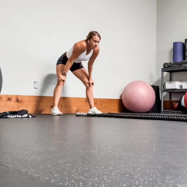 Woman catching breath after workout in a gym room with fitness equipment.