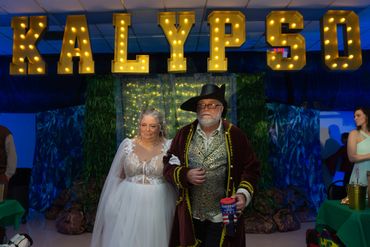 Couple dressed in elaborate costumes under illuminated Kalypso sign.