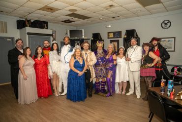 Group of people in formal and costume attire posing indoors.