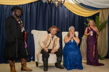 Four people dressed in formal and themed attire posing indoors.