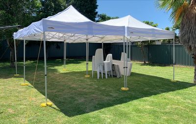White outdoor tents with stacked chairs and tables on green grass under clear blue sky.