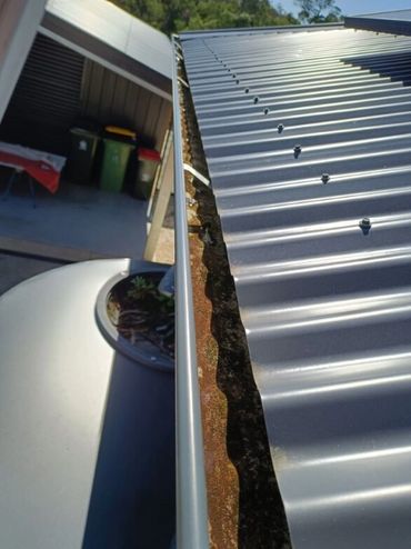 Close-up of a metal roof gutter with visible dirt and rust buildup.