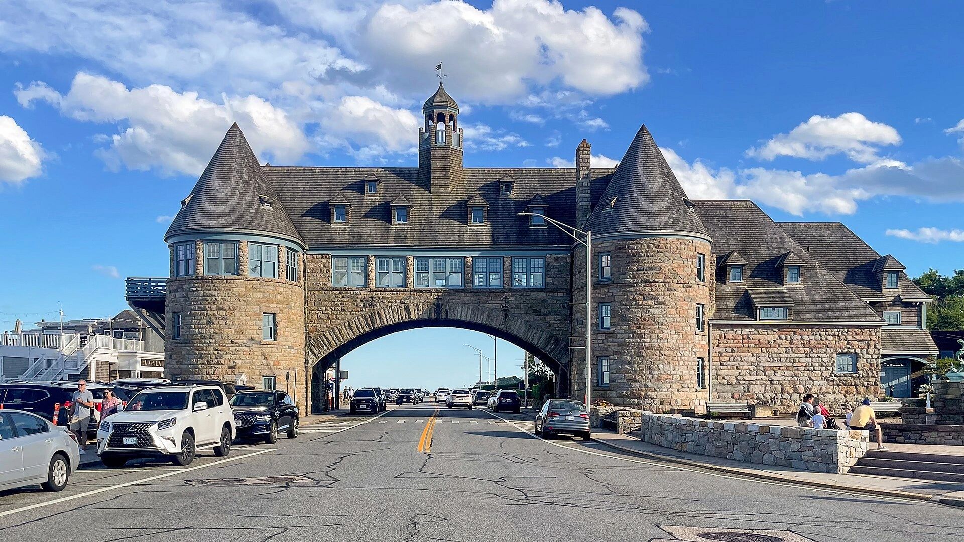Stone building with arch over road and cars passing below.