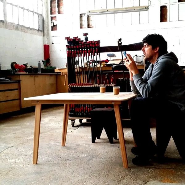 Hombre sentado en taller con dos cafés y celular.