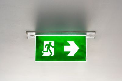 A green emergancy exit sign hanging from the ceiling in an office building. This is to demonstrate t