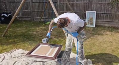 Man spray painting a wooden frame outdoors on a cloth.
