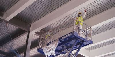 Worker in safety gear on a lift inside an industrial building.