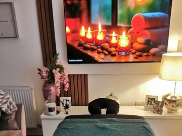 Cozy massage room with calming decor and a serene candlelit image on the TV.