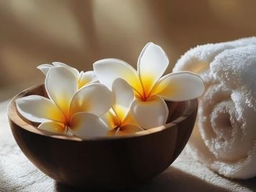Frangipani flowers in a wooden bowl beside rolled towels.