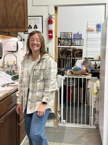 A woman smiling in a casual indoor setting with shelves and a baby gate.