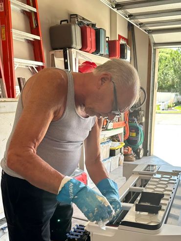 Man wearing blue gloves working on a machine in a garage.