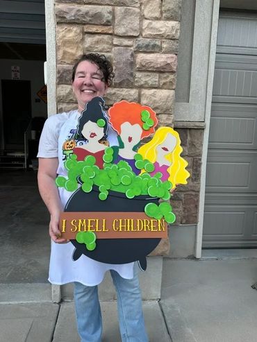 Woman holding a Halloween sign with witches and green bubbles.