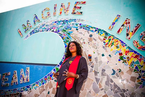 Graduate stands proudly in front of colorful mural with inspirational words.