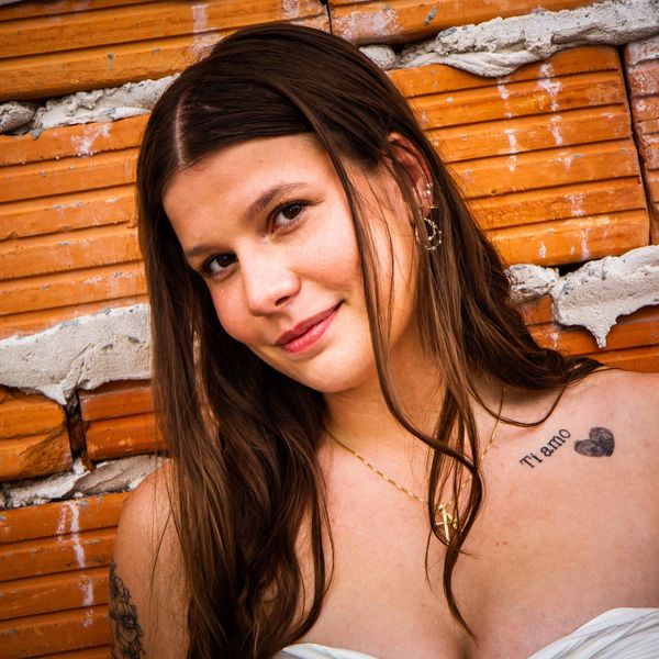 Young woman smiling with a tattoo and brick wall background.