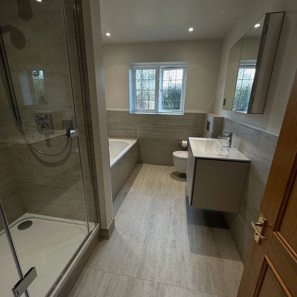 Modern bathroom with shower, bathtub, floating sink, and natural light from window.