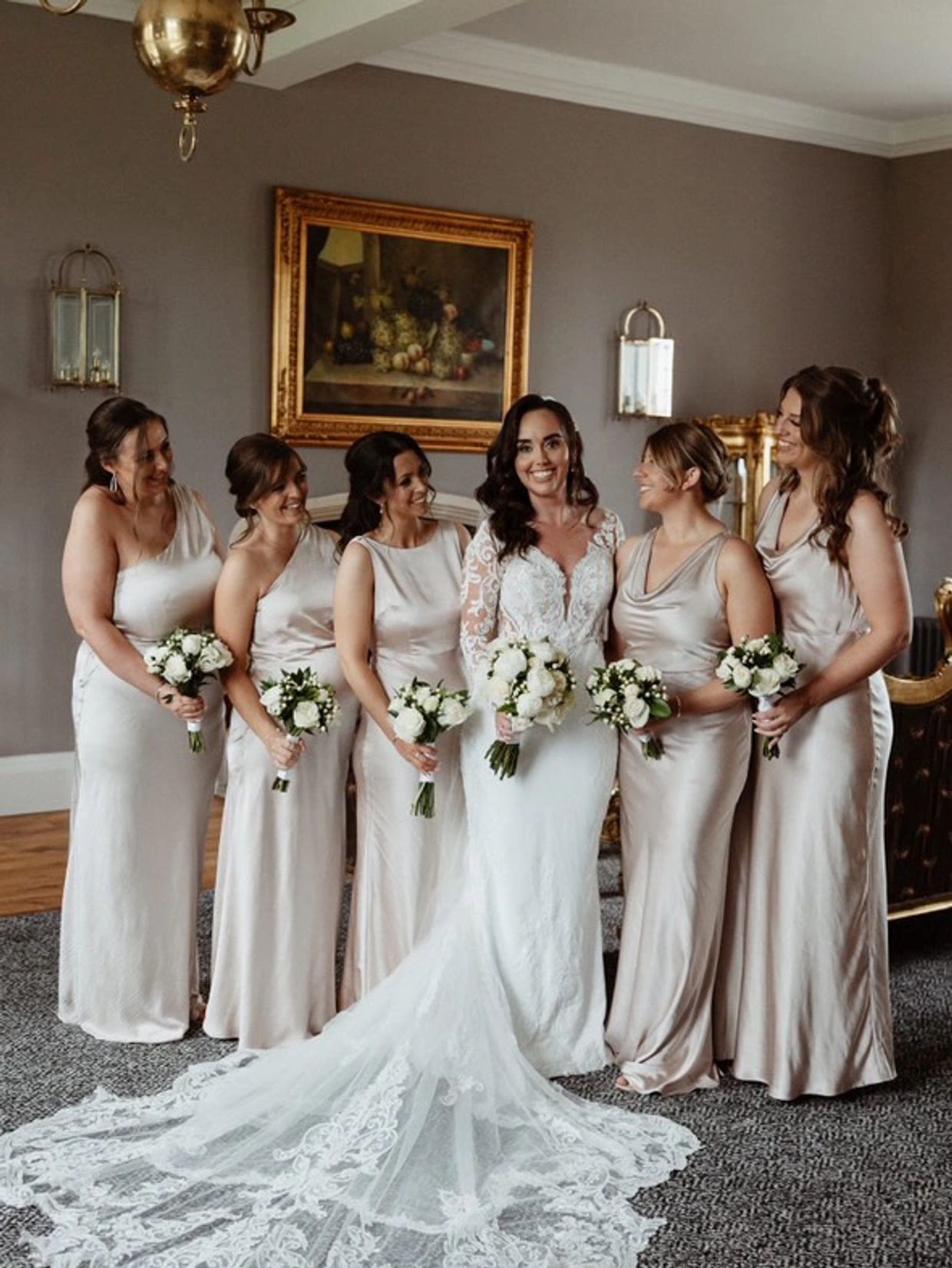 Bride with bridesmaids in elegant dresses holding bouquets indoors.