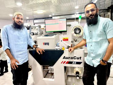 Two men standing beside an AuraCut A6 cutting machine inside a modern facility.