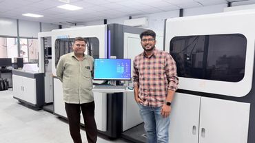 Two men standing beside a large industrial machine with a computer interface.