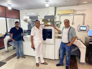 Three men standing in front of a large industrial machine inside a room.