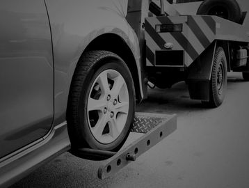 A car being towed by a blue tow truck on a street.