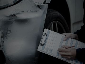 Person inspecting and documenting car damage on a clipboard.
