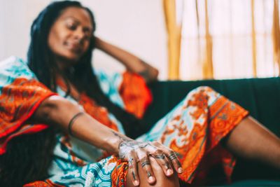 Woman in colorful dress relaxing on a couch with her hand extended forward.