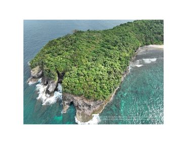 Lush green island with rocky cliffs surrounded by clear blue ocean water.