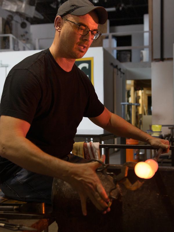 Glassblower Leo Lex working at the bench using diamond sheers on glowing, molten glass