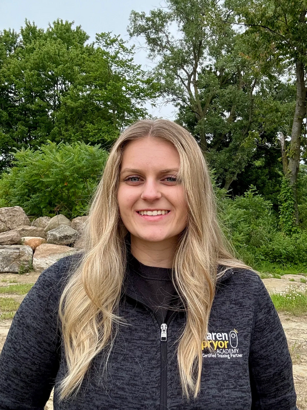Smiling woman with long blonde hair outdoors in a black jacket.