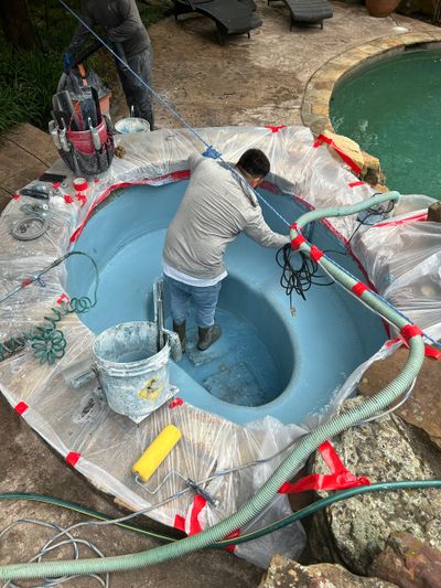 Worker refinishing a small pool or spa with protective plastic coverings around.