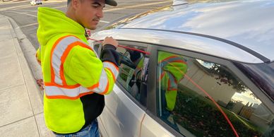 Man in safety vest unlocking a car door with a tool.