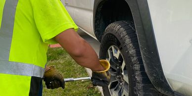 A man in a neon yellow shirt changes a tire on a white truck.