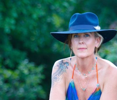 Woman in a blue hat and colorful dress with a tattoo on her shoulder.
