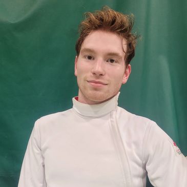 Young man with tousled hair wearing a white turtleneck against a green background.