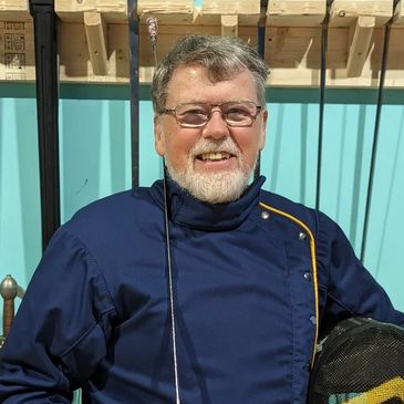 Smiling man in fencing gear holding a foil and mask.